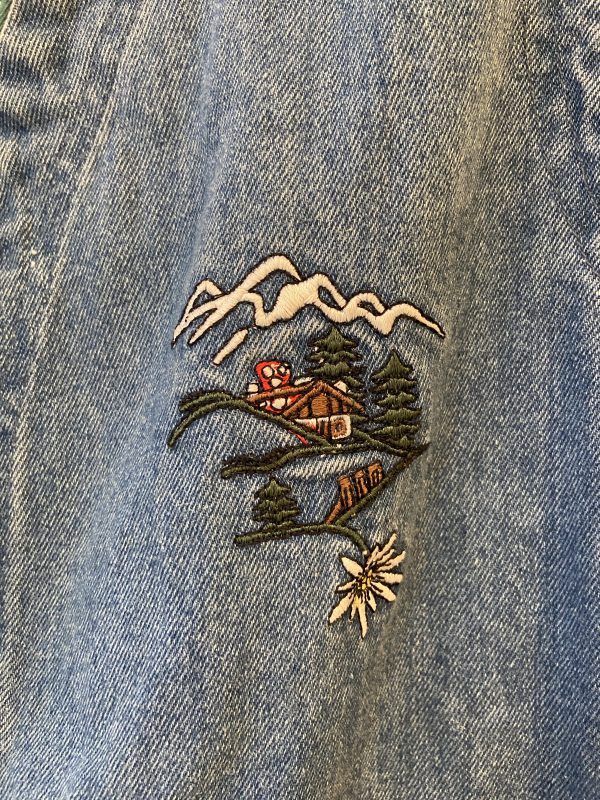 Close-up of vibrant Alpine mountain embroidery on 1970s folk-inspired denim vest