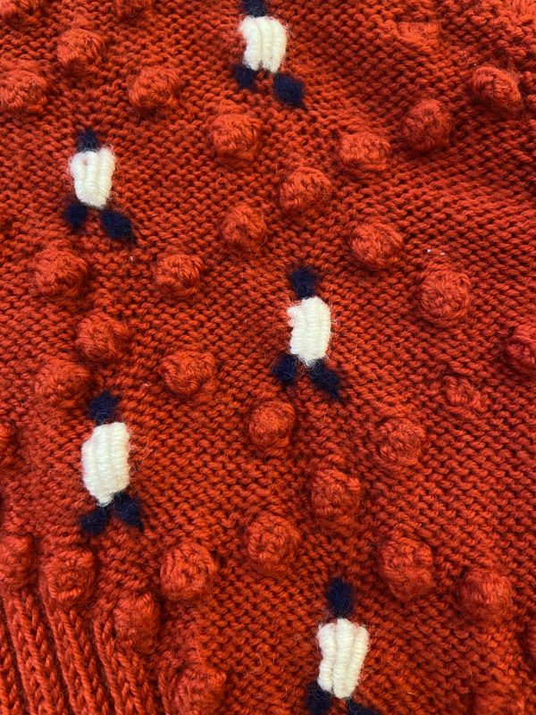 Close-up of white and navy floral embroidery and ornate vintage metal button on 1940s red cardigan