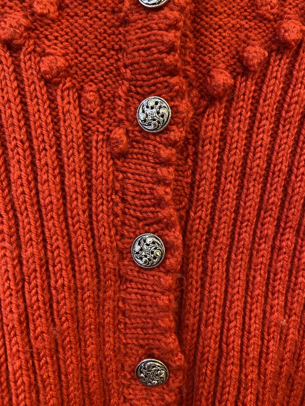 Close-up of white and navy floral embroidery and ornate vintage metal button on 1940s red cardigan