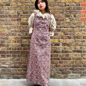 Model wearing late 1960s paisley maxi dress with square neckline and flared skirt in burnt orange and navy