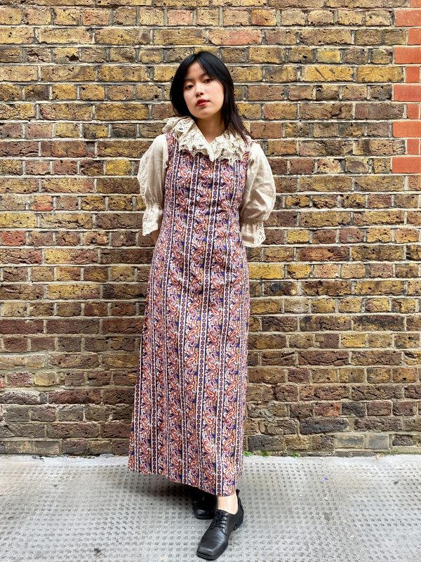 Model wearing late 1960s paisley maxi dress with square neckline and flared skirt in burnt orange and navy