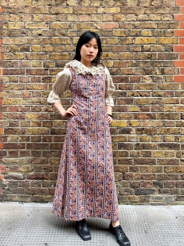 Model wearing late 1960s paisley maxi dress with square neckline and flared skirt in burnt orange and navy