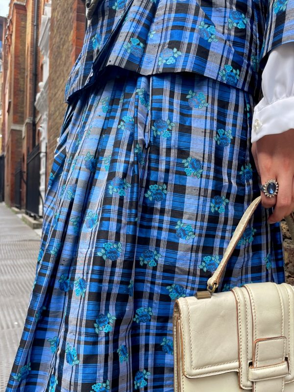Close-up of the waistband and sharp pleats on early 1980s silk check skirt in vibrant tartan with floral accents.