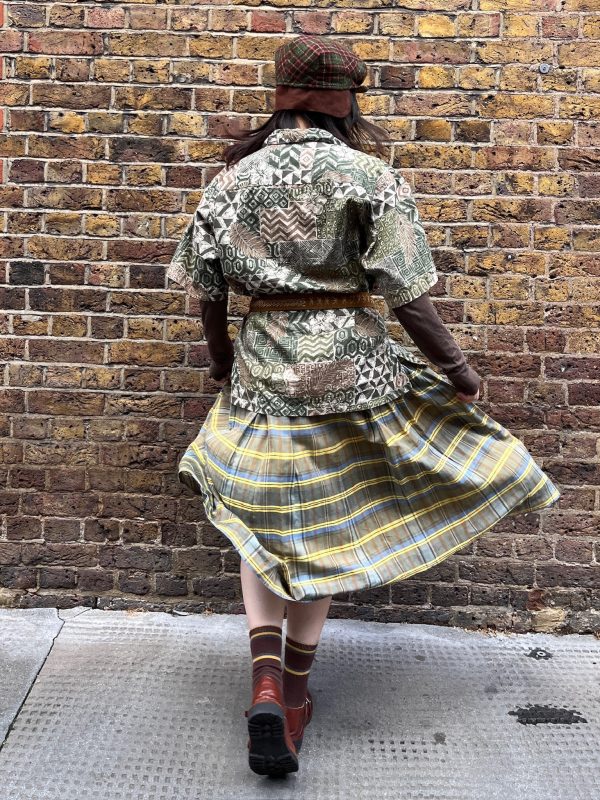 Model wearing a 1970s wool-blend skirt by Bogner in yellow, blue, and brown check with knife pleats and high waist.