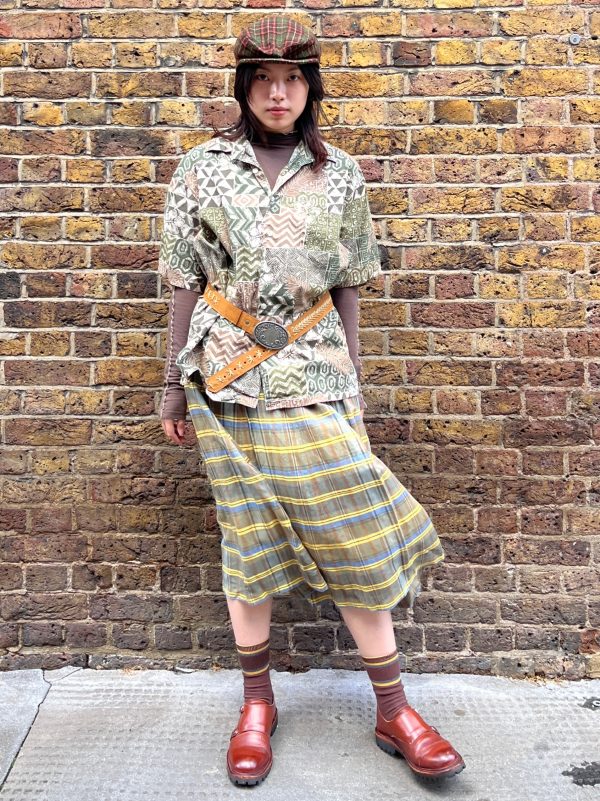 Model wearing a 1970s wool-blend skirt by Bogner in yellow, blue, and brown check with knife pleats and high waist.