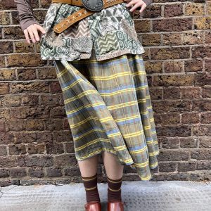 Model wearing a 1970s wool-blend skirt by Bogner in yellow, blue, and brown check with knife pleats and high waist.