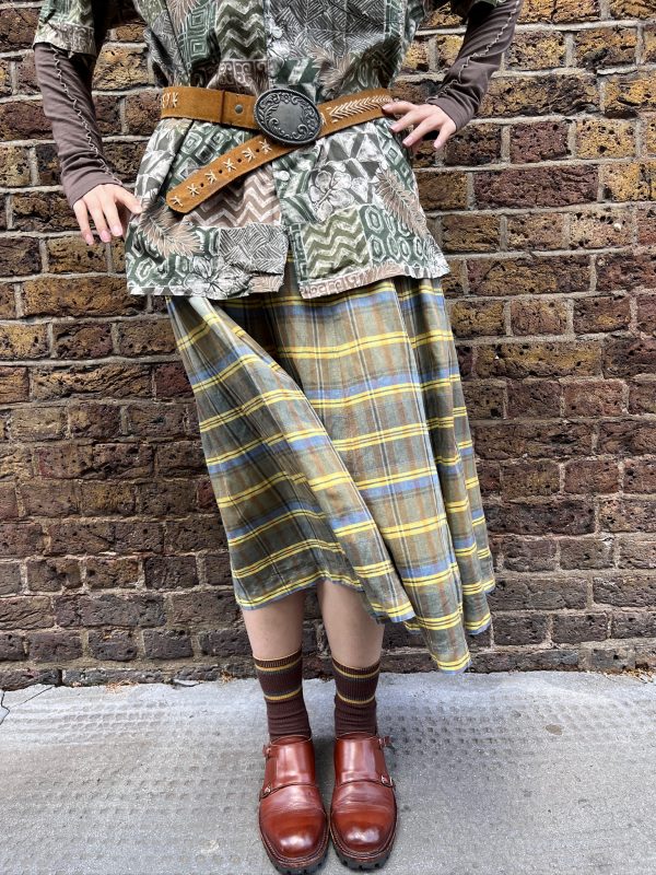 Model wearing a 1970s wool-blend skirt by Bogner in yellow, blue, and brown check with knife pleats and high waist.