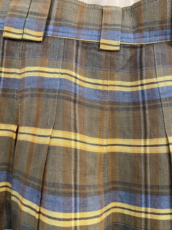 Close-up of the pleated check fabric on a 1970s wool-blend skirt, showing earthy tones and soft texture.